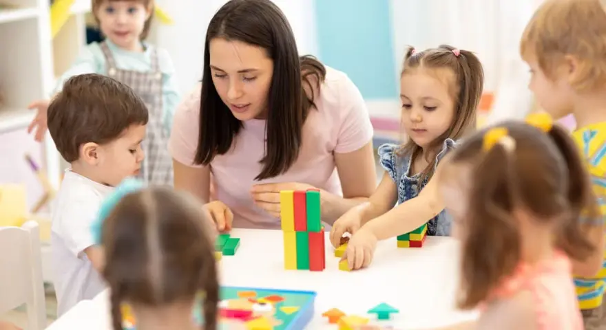 Une enseignante, experte en psychopédagogie à distance, guide des enfants jouant avec des blocs colorés.