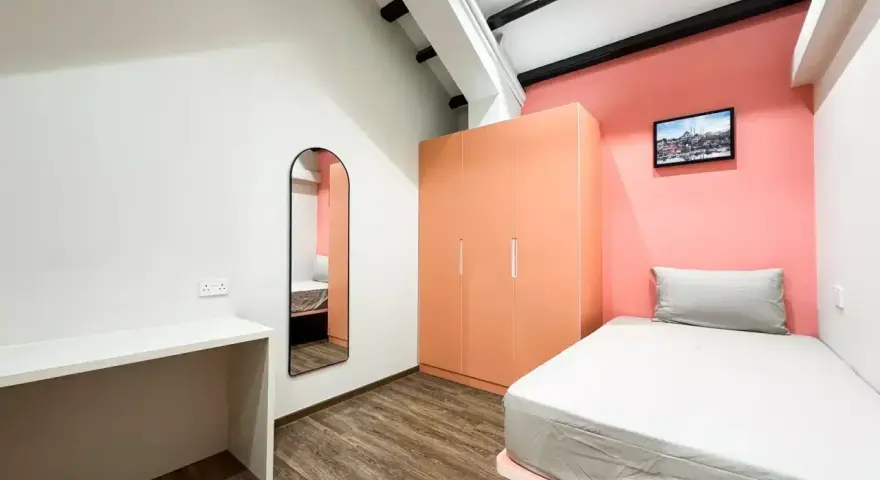 Chambre moderne pour **logement étudiant à Singapour** : lit, bureau, armoire corail et miroir mural.