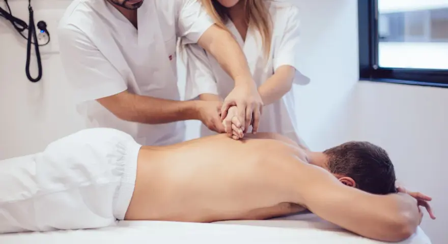 Des étudiants de l'école kine Gérone apprennent la kinésithérapie en pratiquant sur un patient allongé.