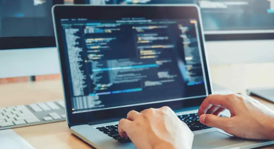 Des mains tapant sur un clavier d'ordinateur portable affichant du code. Une opportunité de formation informatique sans bac pour un avenir prometteur.