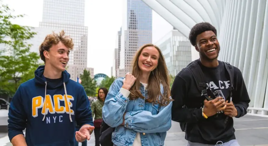 Trois étudiants souriants marchent dans le quartier financier de New York, un lieu idéal pour un MBA.
