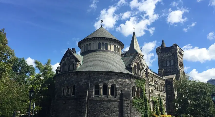 Bâtiment historique en pierre, rappelant une école de cinéma à Toronto, sous un ciel bleu et nuageux.