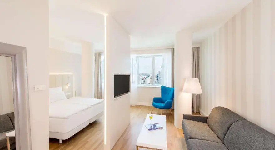 Chambre moderne avec lit, canapé, TV et vue sur la ville. Idéal pour un logement étudiant à Vienne, Autriche.