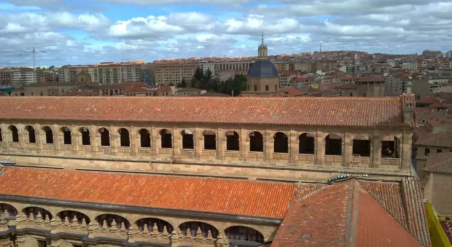 Vue aérienne de l'université pontificale de Salamanque, avec ses toits de tuiles rouges et son dôme emblématique sous un ciel nuageux.