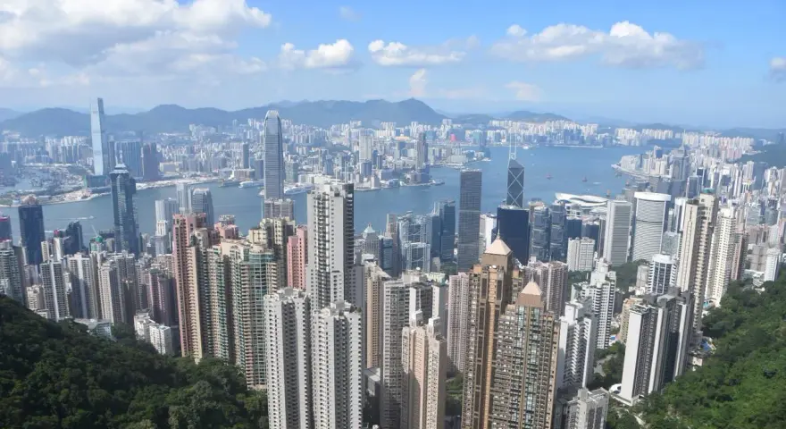 Vue panoramique de Hong Kong, avec ses gratte-ciel s'étendant jusqu'à l'horizon. On aperçoit le campus de la Hong Kong Baptist University, niché au milieu de la verdure luxuriante.