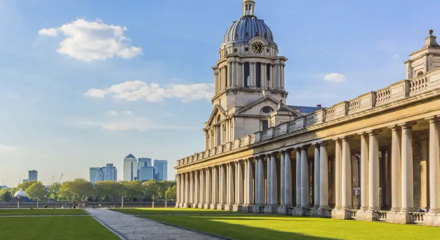 Le bâtiment néoclassique de l'université de Greenwich, avec son dôme et ses colonnes imposantes, se dresse sous un ciel bleu clair.