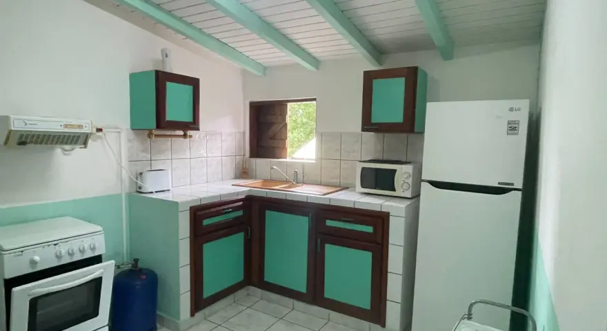 Cuisine fonctionnelle pour un logement étudiant en Guadeloupe : cuisinière, réfrigérateur, micro-ondes, évier et rangements.