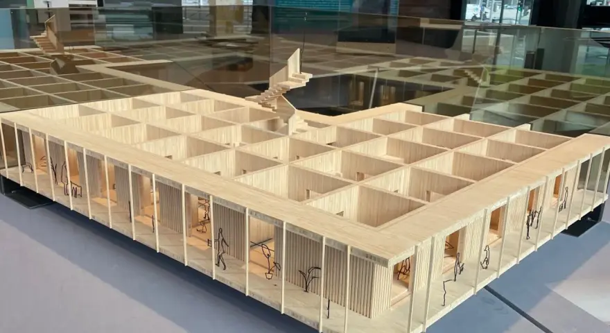 Maquette en bois d'une école d'architecture belge, avec des figures stylisées et des plantes.