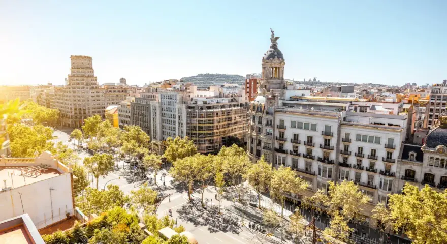 Vue aérienne de Barcelone, ville dynamique qui pourrait figurer dans le classement université espagne. Bâtiments haussmanniens, arbres luxuriants et ciel bleu.