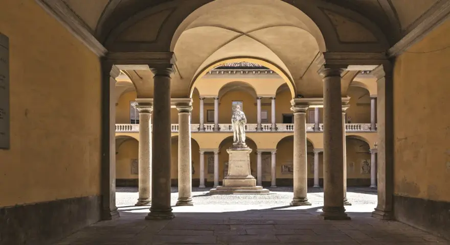 Cour intérieure de l'université de Pavie, avec une statue au centre, entourée d'arcades et de colonnes.