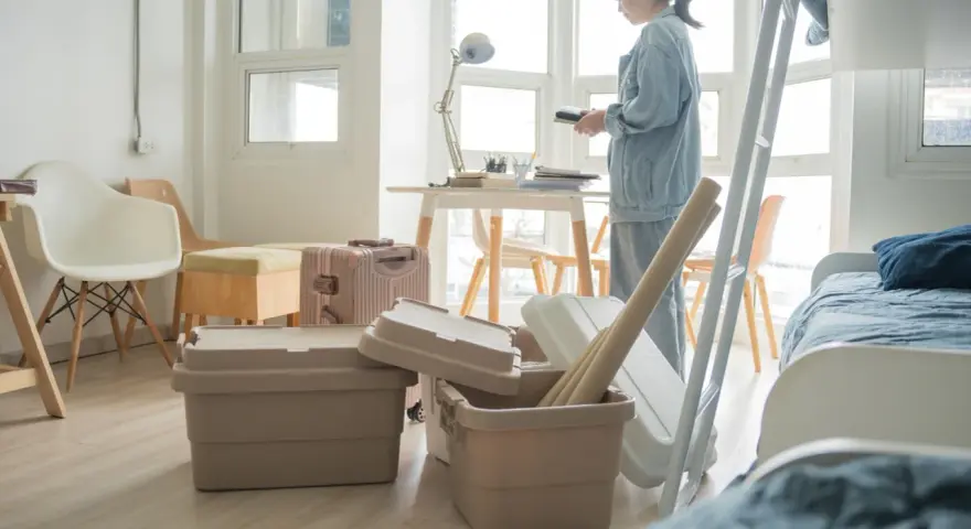 Une jeune femme déballe ses affaires dans une chambre d'étudiant au Canada. Valises et boîtes sont empilées, prête pour une nouvelle vie.