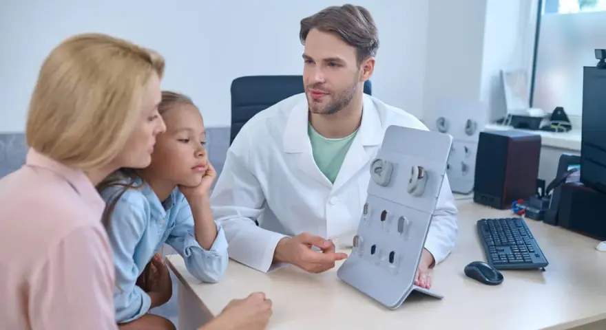 Un audioprothésiste explique des appareils auditifs à une mère et sa fille. Une scène qui pourrait illustrer la formation accélérée audioprothésiste.