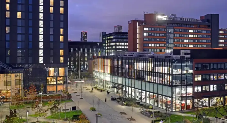 Bâtiments modernes illuminés le soir, avec une enseigne Alliance Manchester Business School visible.