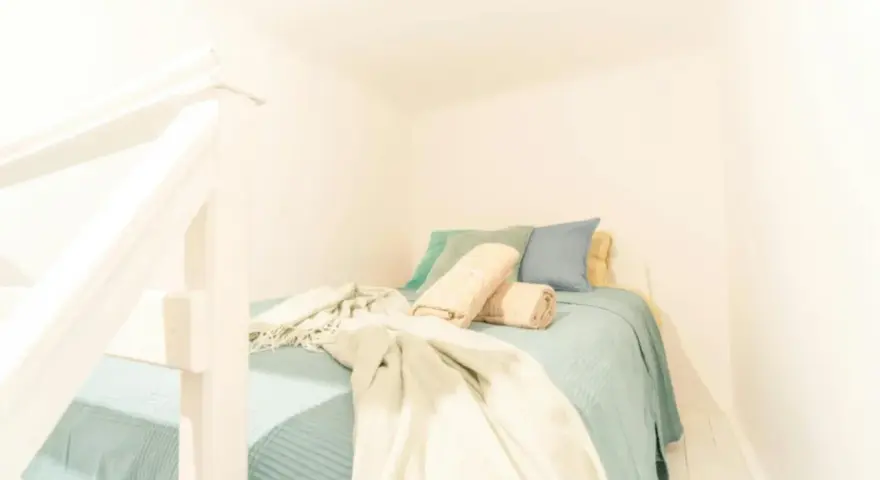 Lit douillet dans un logement étudiant à Budapest, avec des coussins bleus et verts, et des plaids beiges.