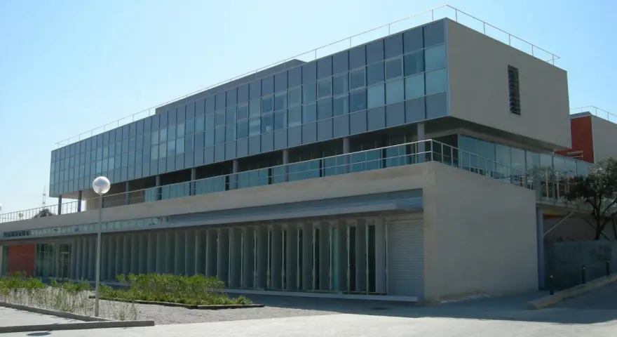 Bâtiment moderne aux lignes épurées, possiblement une école d'élite à Madrid, avec de grandes baies vitrées et une façade en pierre claire.