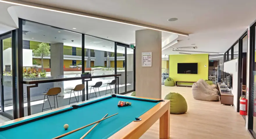 Salle commune moderne pour logement étudiant à Sydney, avec table de billard, poufs et espace extérieur visible.