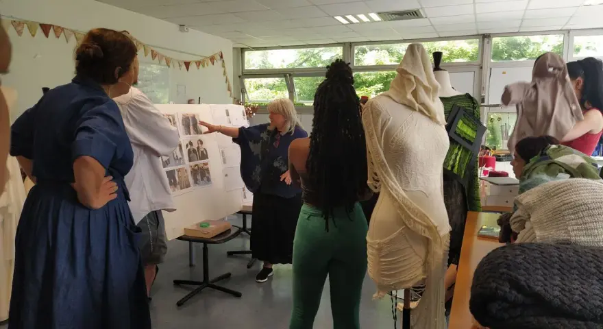 Des élèves d'une école de mode gratuite présentent leurs créations sur des mannequins. Une enseignante explique un tableau d'inspiration.