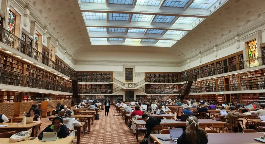 Vaste bibliothèque avec étudiants travaillant sur leurs ordinateurs portables, un décor idéal pour une licence science politique à distance.