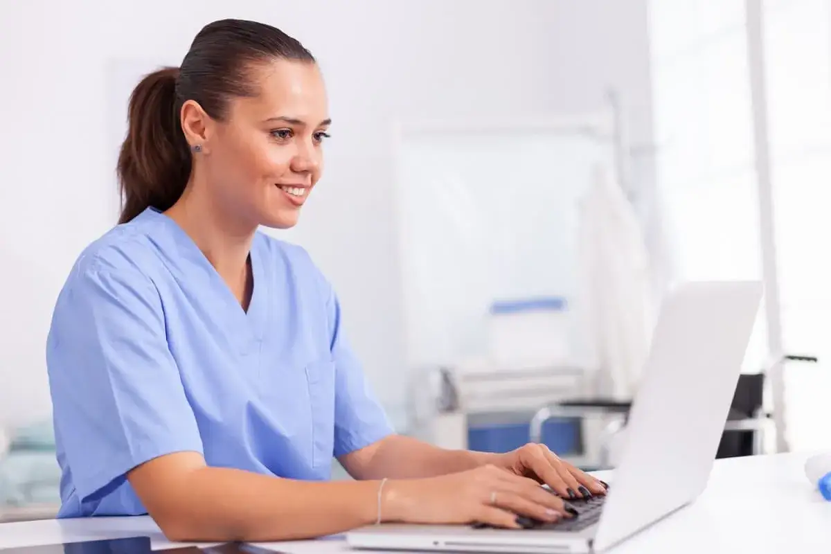 Une infirmière souriante travaille sur son ordinateur portable, offrant des conseils de santé en ligne.