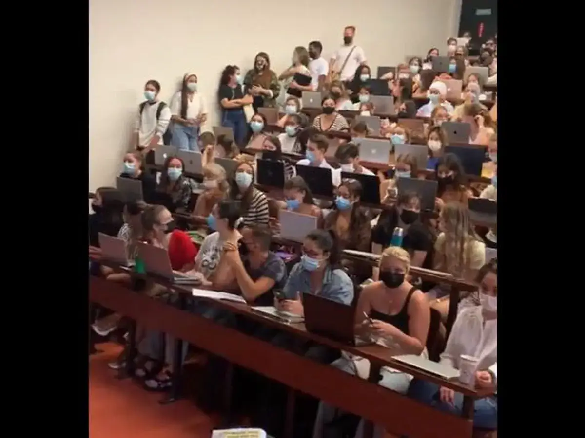 Des étudiants en amphithéâtre, masqués, concentrés pour étudier la psychologie. Ordinateurs portables ouverts, prêts à noter les cours.