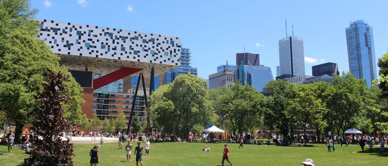 Un parc anim&eacute; &agrave; Toronto, avec des &eacute;tudiants de la Toronto Film School profitant du soleil pr&egrave;s de b&acirc;timents modernes.