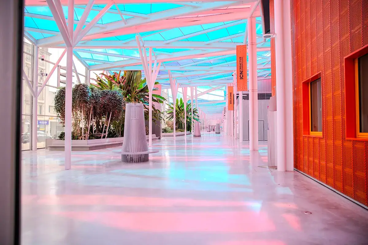 Allée lumineuse de l'ICN Business School, avec des plantes luxuriantes et des bannières orange.