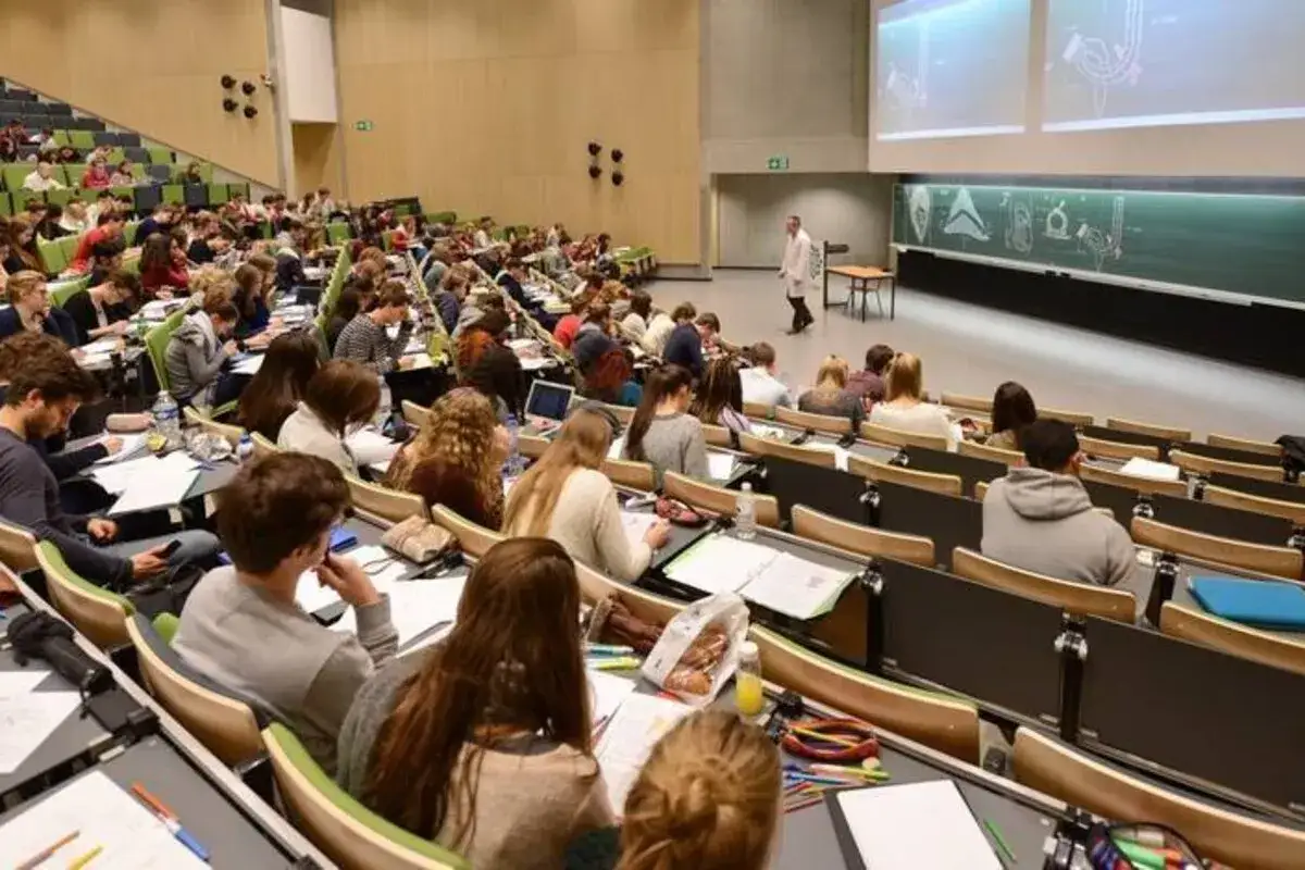 Amphithéâtre bondé pour une formation en Belgique. Des étudiants attentifs prennent des notes, un professeur donne cours.