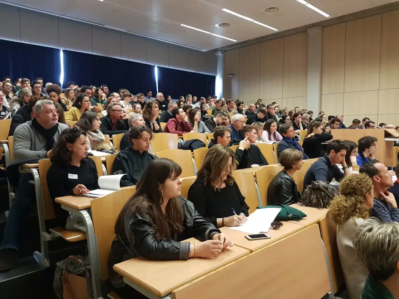Amphithéâtre rempli d'étudiants attentifs, certains prenant des notes. Une scène typique d'une école kine suisse.