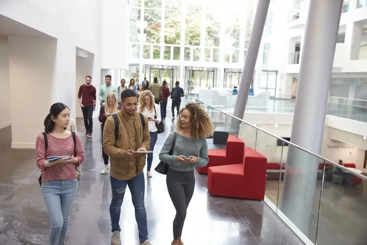 Étudiants diversifiés dans un hall moderne, discutant et se déplaçant. Un groupe se dirige vers une grande verrière, symbolisant l'ouverture et la relation internationale etude.