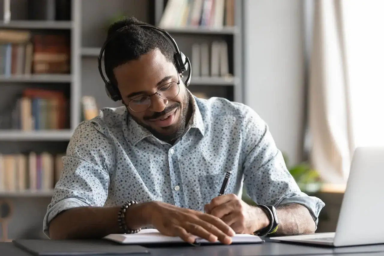 Un étudiant concentré suit son cours de msc finance online, casque sur les oreilles, prenant des notes.