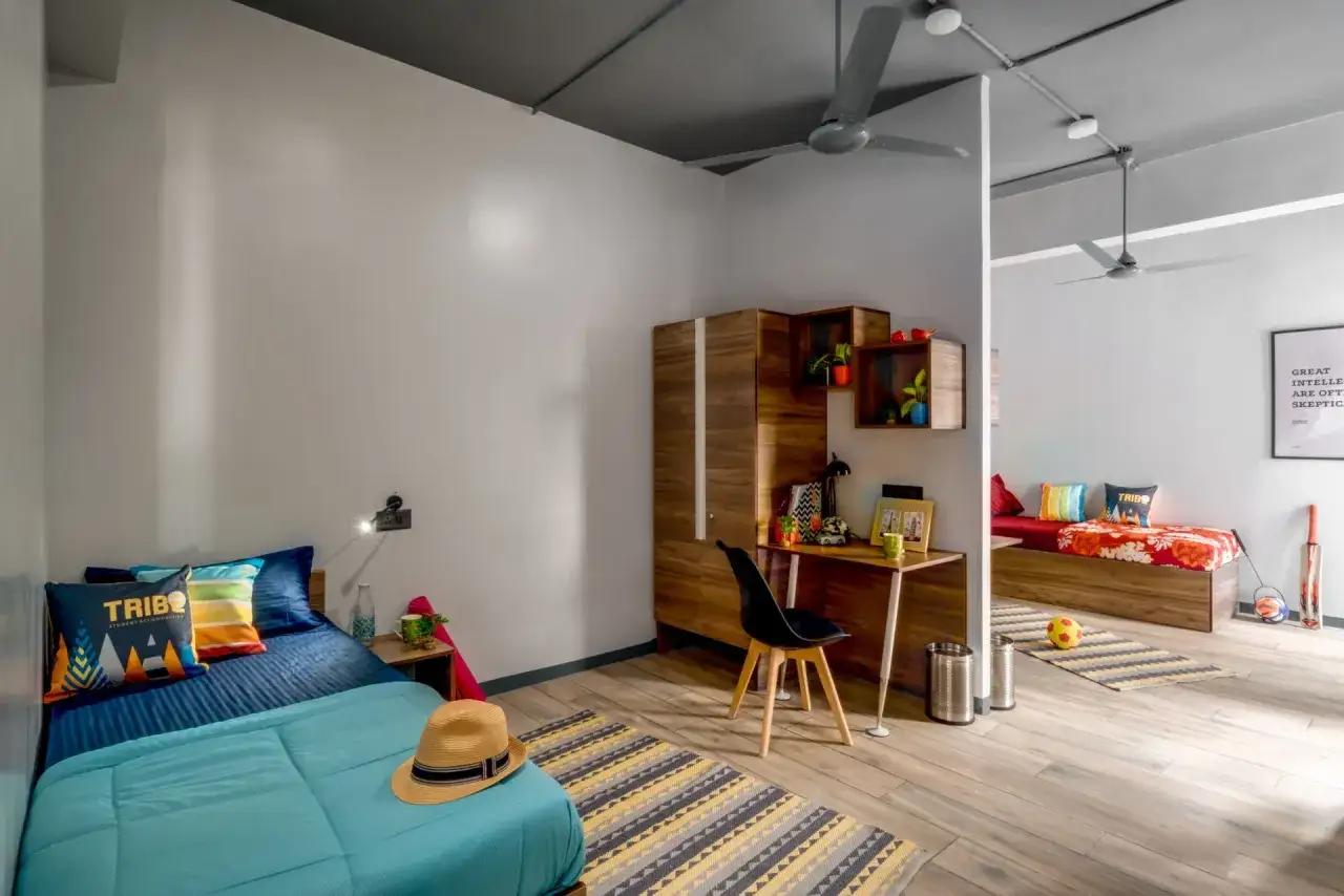 Chambre moderne avec deux lits, bureau et armoire en bois. Un aperçu du coût de la vie en Inde, avec des touches de couleur vives.