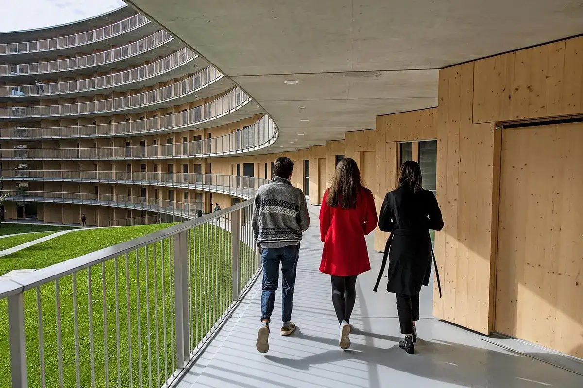 Trois &eacute;tudiants marchent dans un couloir moderne de l'universit&eacute; de Gen&egrave;ve, un b&acirc;timent prim&eacute; pour son architecture.