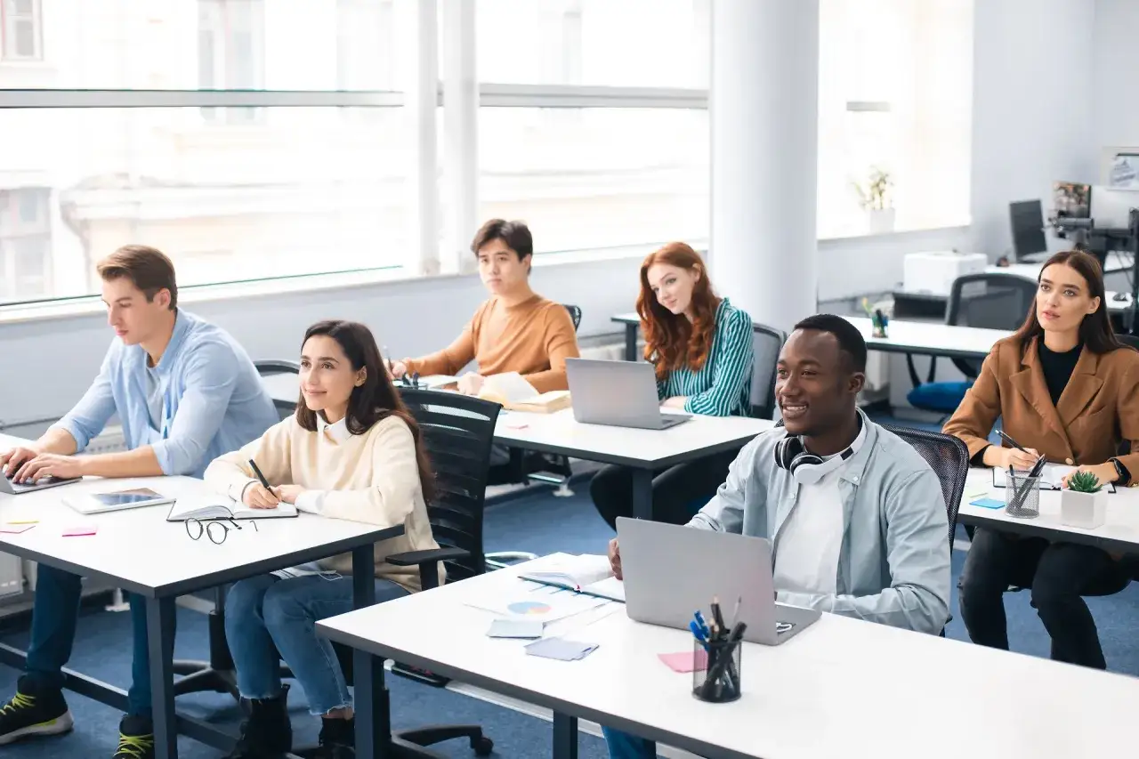 Des étudiants en salle de classe, certains travaillent sur leurs ordinateurs portables. Ils semblent suivre un cours sur le master finance quantitative classement.