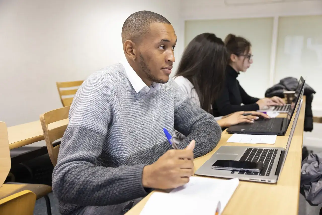 Des &eacute;tudiants suivent des programmes MBA en ligne, concentr&eacute;s sur leurs ordinateurs portables dans une salle de classe.