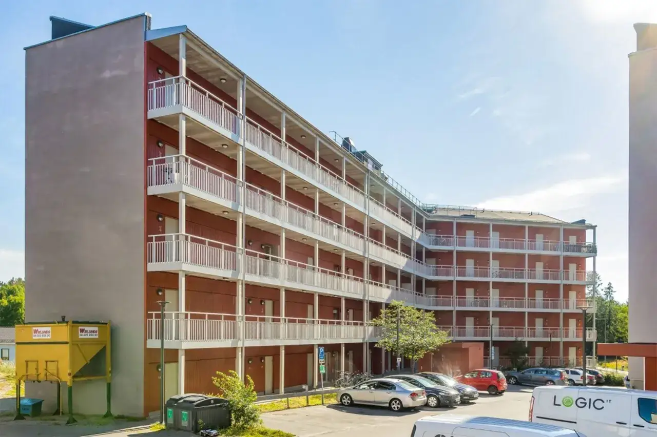 Immeuble moderne avec balcons, offrant un logement étudiant à Stockholm. Des voitures sont garées devant.
