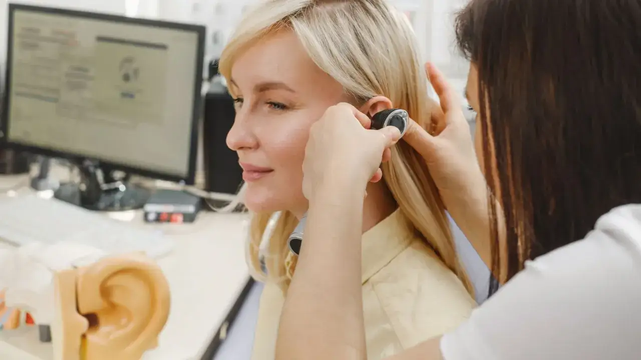 Une audioproth&eacute;siste ajuste un appareil auditif. Une formation audioproth&eacute;siste &agrave; distance est possible pour apprendre ce m&eacute;tier.