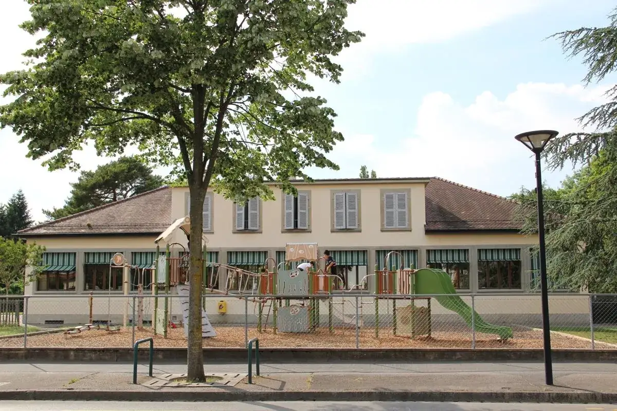Aire de jeux d'une &eacute;cole suisse &agrave; Gen&egrave;ve, avec un toboggan vert et des enfants qui jouent.