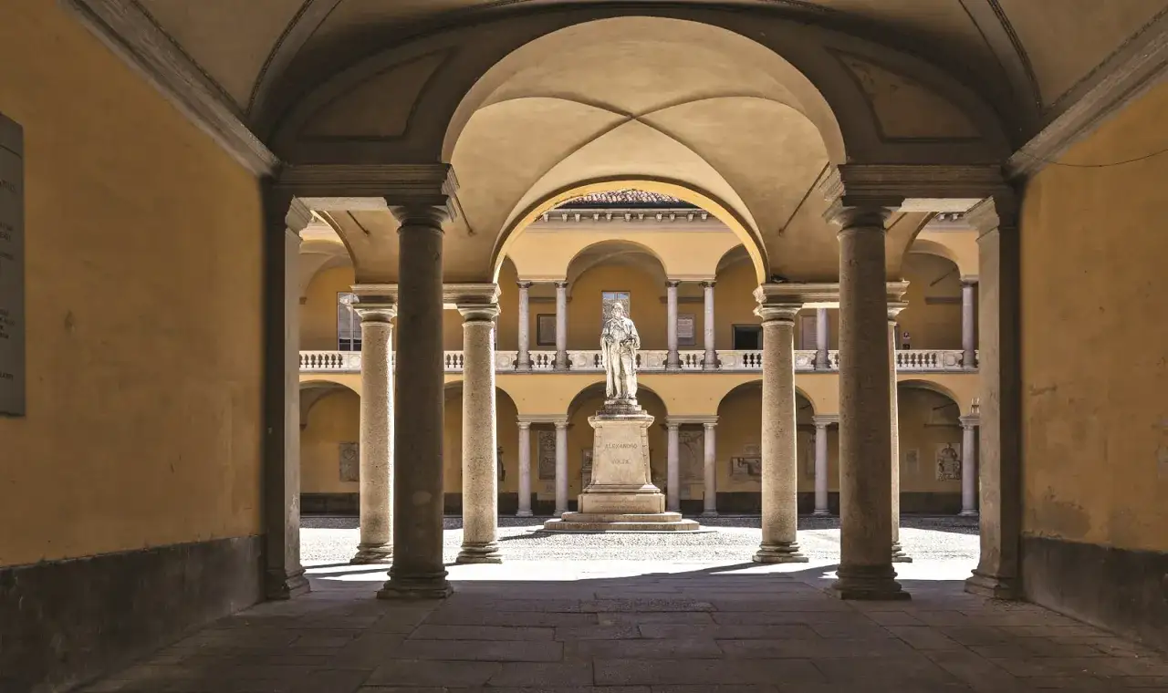 Cour intérieure de l'université de Pavie, avec une statue au centre et des arcades.