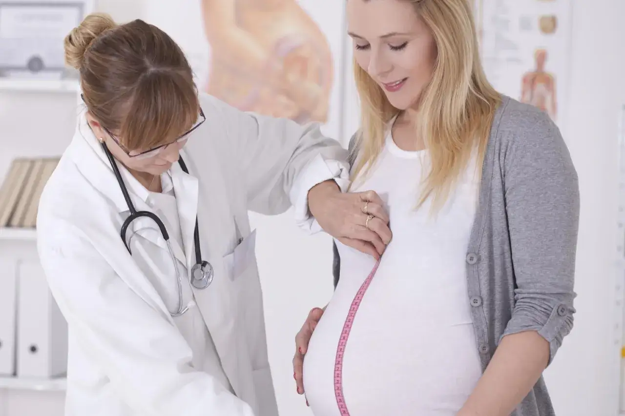 Une sage-femme mesure le ventre d'une femme enceinte. L'image illustre un suivi médical attentif, essentiel dans le cadre d'une etude sage femme.