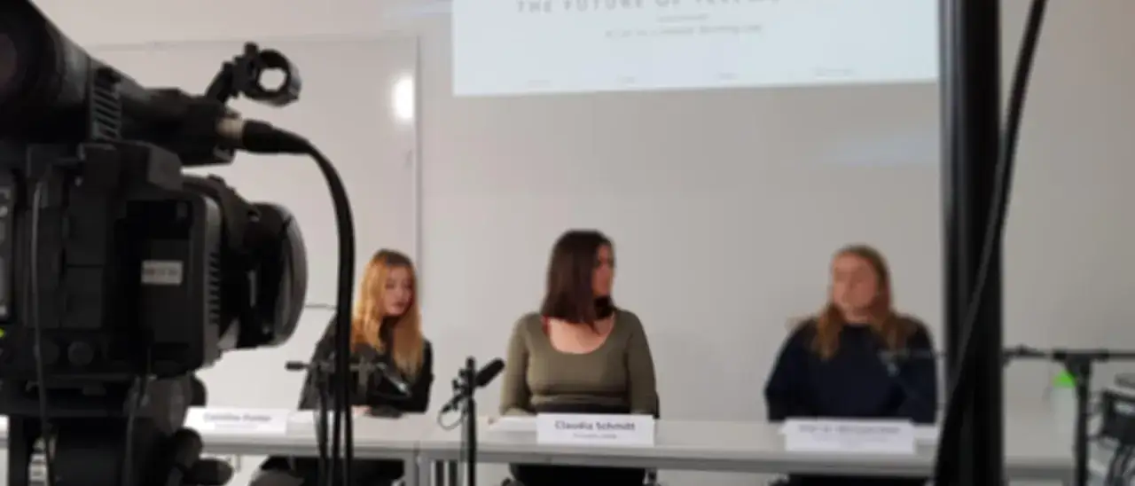 Caméra professionnelle filmant un panel de trois femmes, une experte en relation publique, discutant devant un écran.