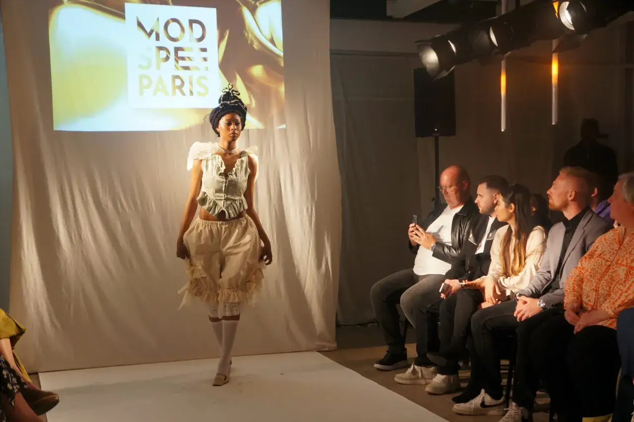 Défilé de mode : une jeune femme présente une tenue originale sur fond d'écran