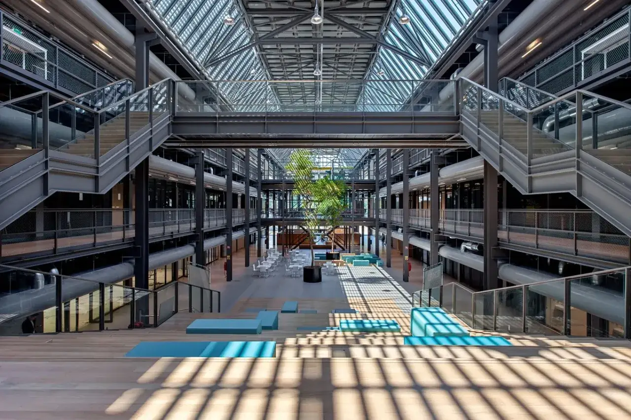 Atrium moderne de l'université de Twente, avec un arbre central, des escaliers métalliques, des passerelles et une verrière lumineuse.