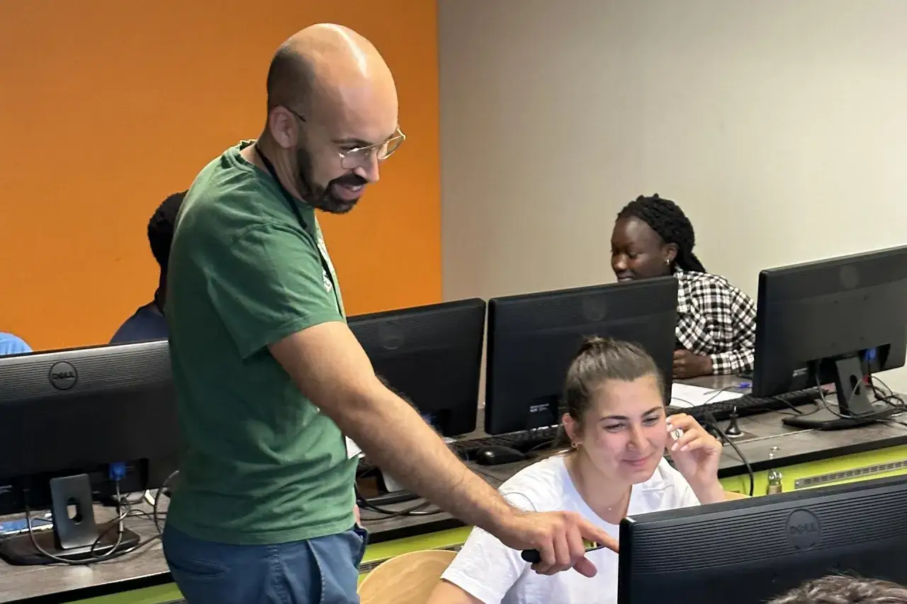 Un formateur guide une jeune femme devant son écran. Une formation informatique sans bac est en cours, ouvrant des portes vers de nouvelles carrières.