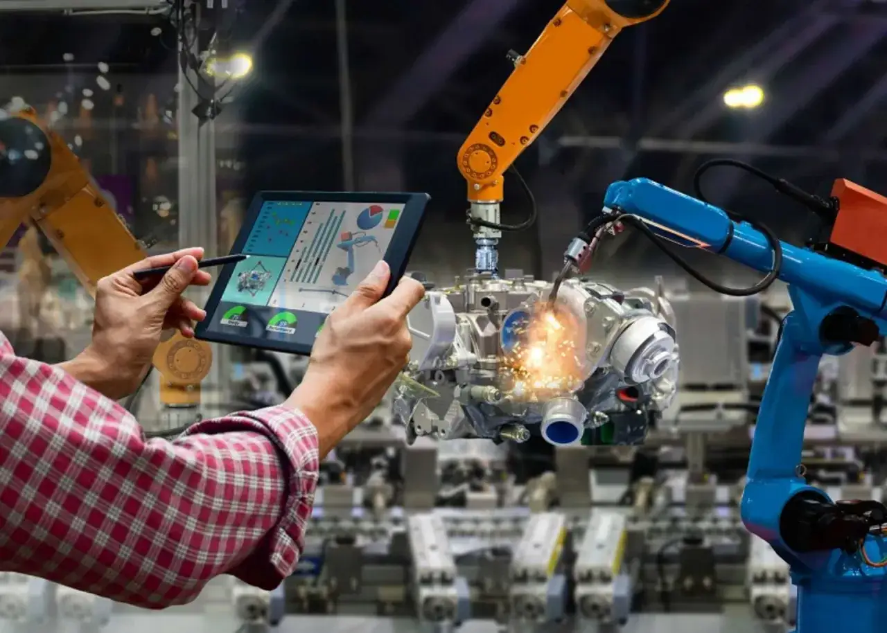 Un opérateur supervise un master genie mécanique sur une tablette, tandis que des bras robotiques assemblent un moteur.
