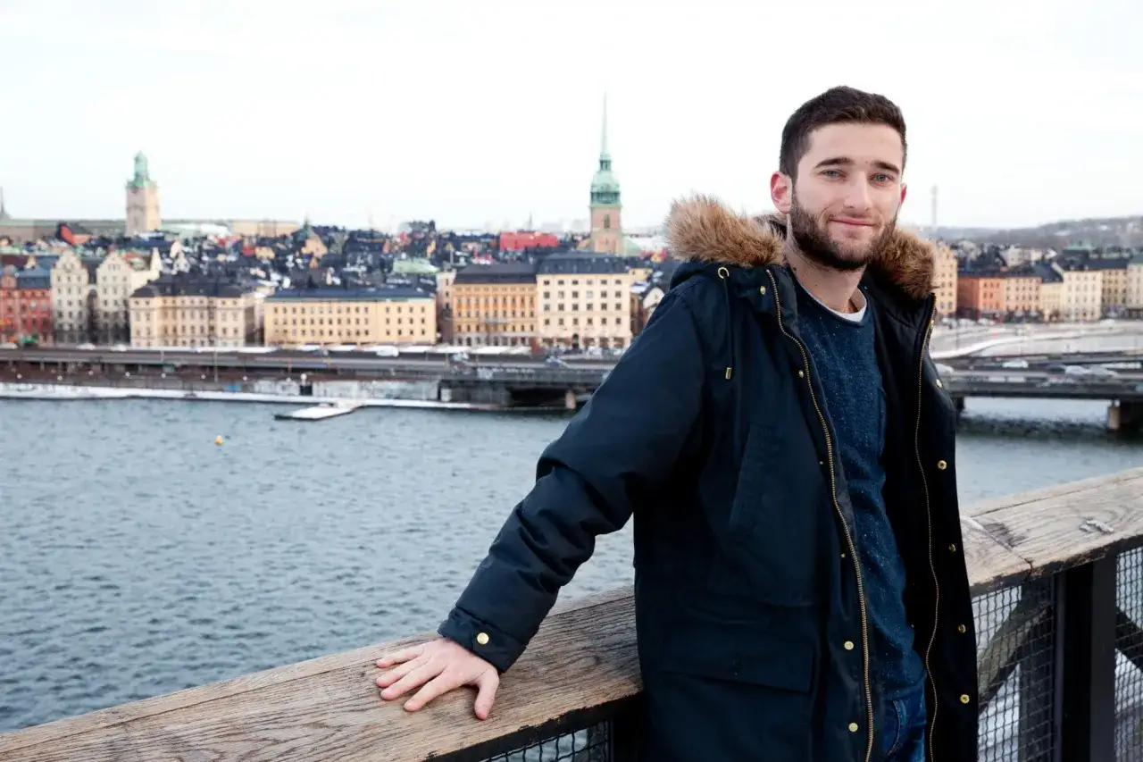 Un jeune homme souriant devant le paysage urbain de Stockholm. Le coût de la vie en Suède est élevé, mais la beauté de la ville en vaut la peine.
