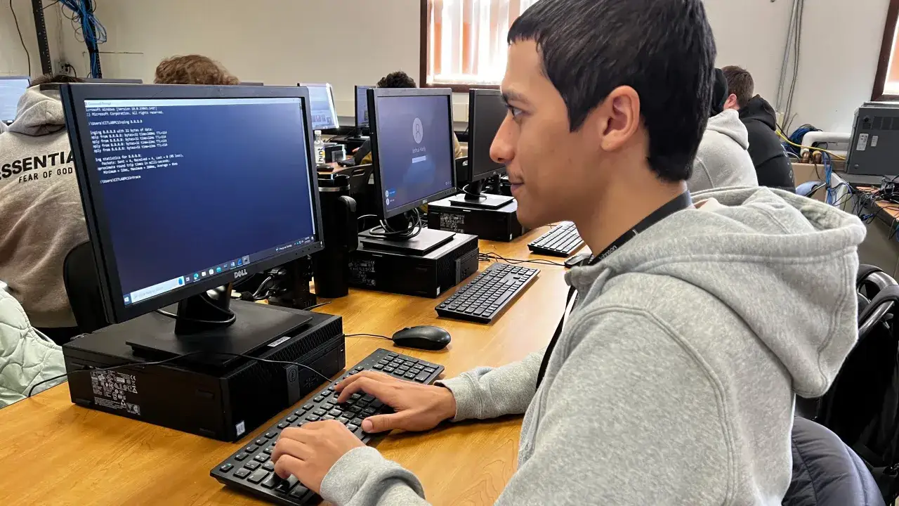 Un jeune homme concentré sur son écran, apprenant à maîtriser la cybersécurité à distance. Il tape sur son clavier, analysant des données réseau.
