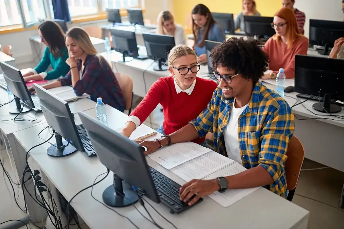 Des étudiants travaillent sur leurs ordinateurs, certains collaborent. L'un d'eux semble suivre un cours de master informatique à distance.