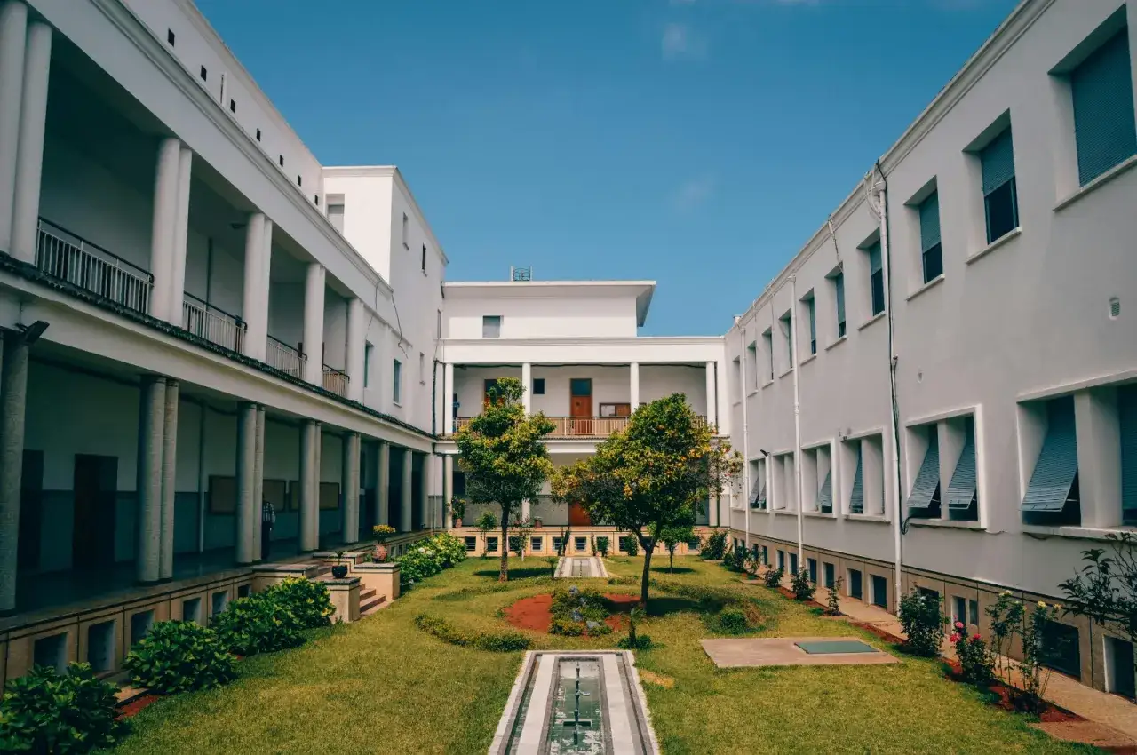 Cour int&eacute;rieure d'un b&acirc;timent blanc, id&eacute;ale pour un &eacute;tudiant fran&ccedil;ais cherchant une aide au logement en Espagne. Jardin verdoyant et ciel bleu.