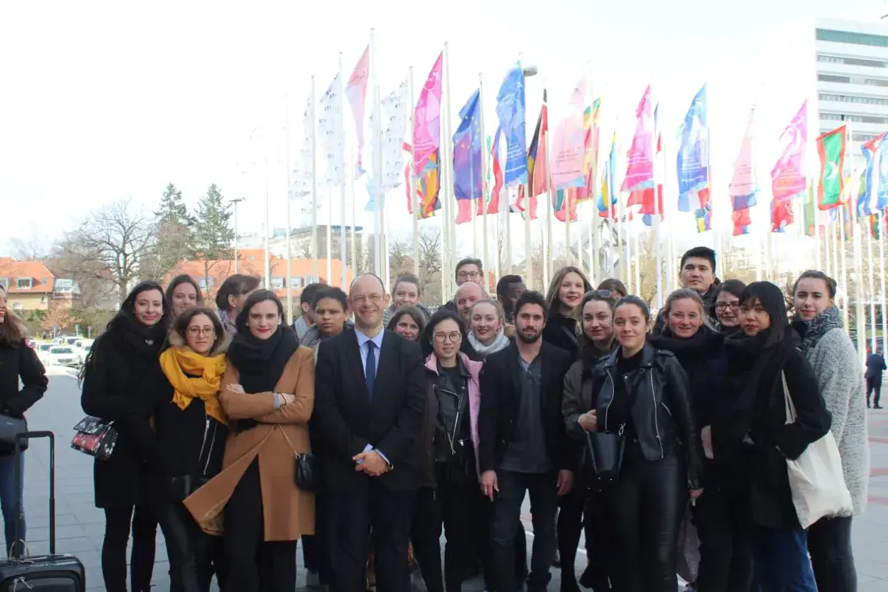Groupe d'&eacute;tudiants souriants devant des drapeaux, pr&ecirc;ts pour leur future carri&egrave;re dans une &eacute;cole de tourisme gratuite.