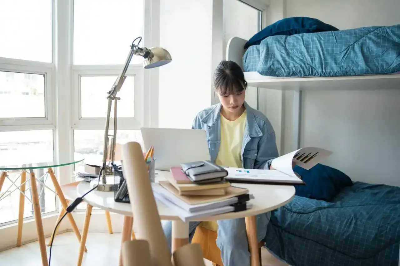 &Eacute;tudiante &agrave; Singapour, elle jongle avec ses &eacute;tudes et le co&ucirc;t de la vie. Son bureau est encombr&eacute; de documents, son ordinateur portable allum&eacute;, et le lit superpos&eacute; t&eacute;moigne de son espace de vie compact.